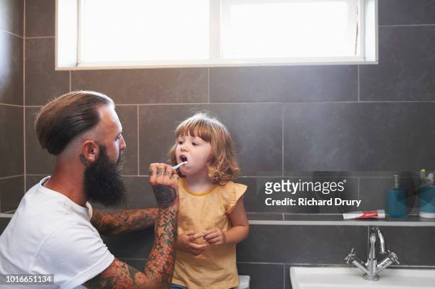 dad brushing toddler daughter's teeth - badezimmer mann stock-fotos und bilder