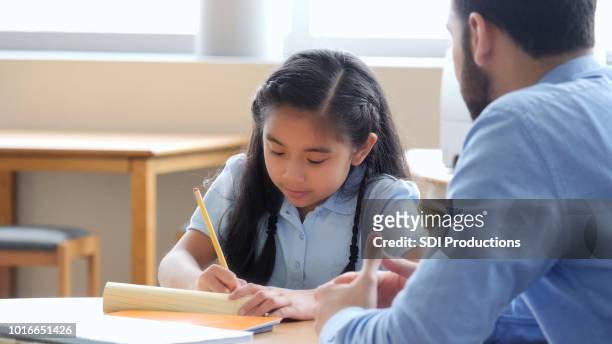 elementary age girl works on homework with her tutor - encouragement stock pictures, royalty-free photos & images