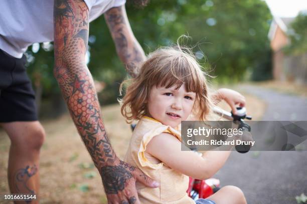 dad helping toddler daughter to ride her tricycle - tricycle stock-fotos und bilder