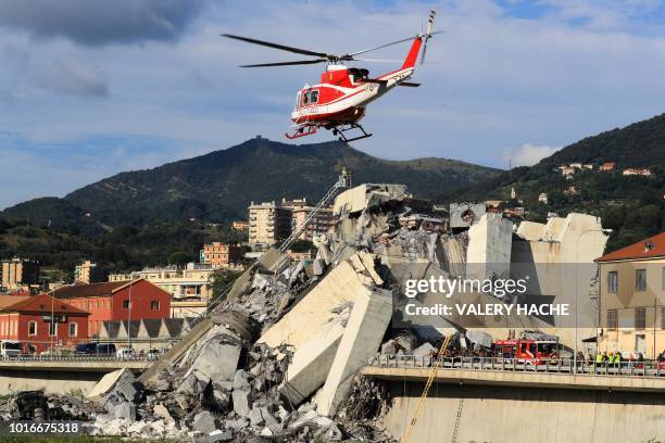 Helicopter hovers as rescuers work at the site where the Morandi motorway bridge collapsed in Genoa on August 14, 2018. - At least 30 people were...