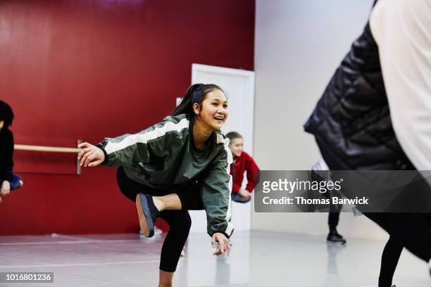 smiling young woman stretching before hip hop dance practice in dance studio - crecimiento estirón fotografías e imágenes de stock