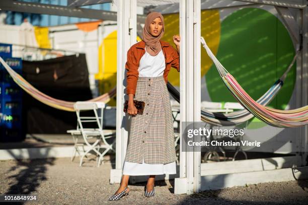 Rawdah wearing checked skirt, white dress, orange jacket, clutch is seen outside Iben during Oslo Runway SS19 on August 14, 2018 in Oslo, Norway.