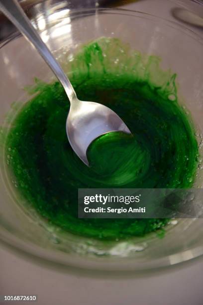 a metal spoon in a bowl containing glue, green food colouring and glitters to make slime - liquid galaxy stock pictures, royalty-free photos & images