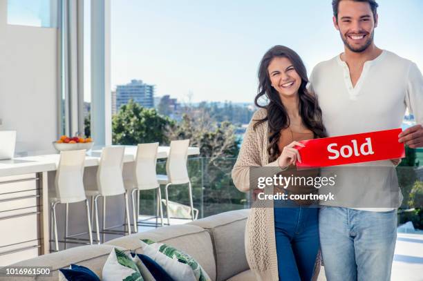 young couple holding a leased rental sign in a luxury home. - real estate sold stock pictures, royalty-free photos & images