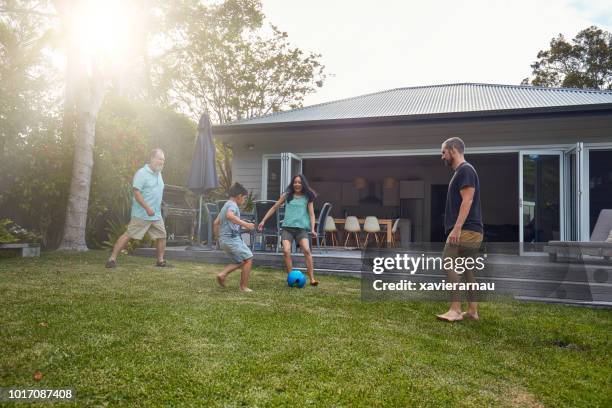 multi-generation family playing soccer on lawn - australian home stock pictures, royalty-free photos & images