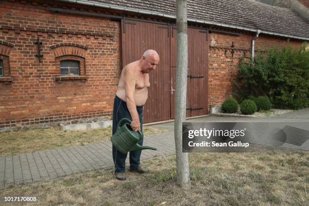 Helmut Kujat waters a tree amongst parched grass in front of his house at the end of the day in the village of Landwehr on August 15, 2018 near...