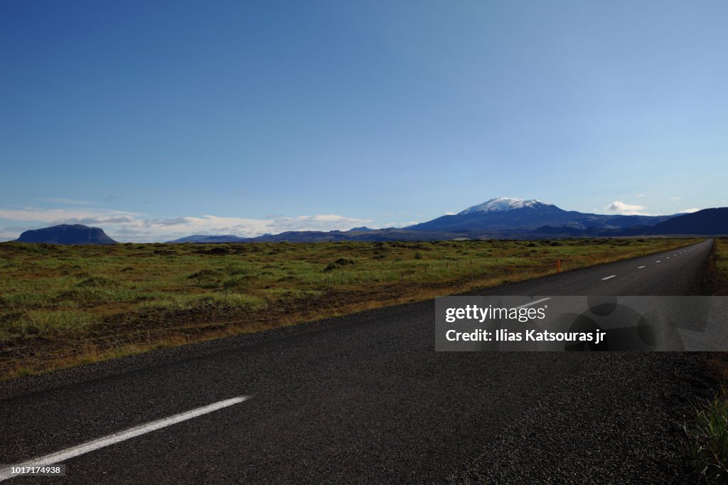 Empty road in Iceland, with mountains and volcano in the background