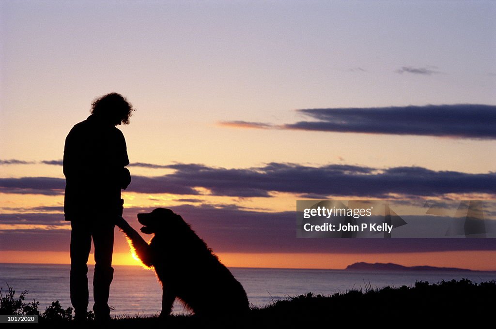 WOMAN AND DOG ON BEACH AT SUNSET