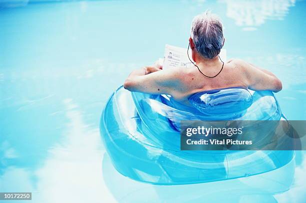 mature man floating in poolchair, reading - bubble chair stock-fotos und bilder