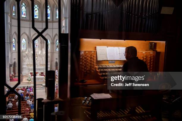 Organist Don Fellows is reflected on a glass encasement as parishioners worship during a mass to celebrate the Assumption of the Blessed Virgin Mary...