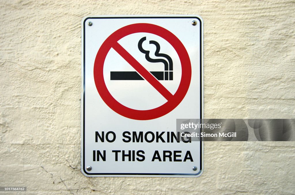 'No Smoking in this area' sign on a building exterior stucco brick wall