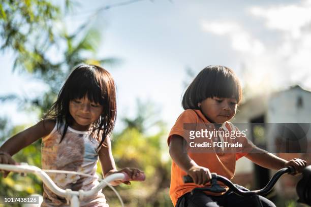 twee kinderen een fiets in een landelijke plaats - village life stockfoto's en -beelden