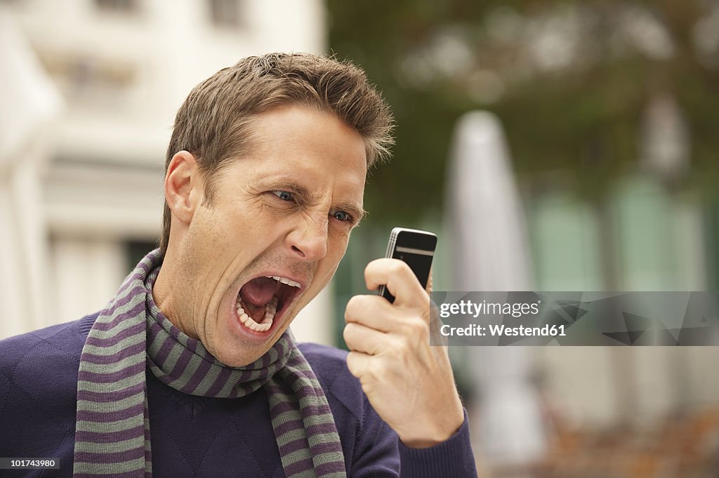 Germany, Bavaria, Munich, Man holding mobile phone, screaming, portrait