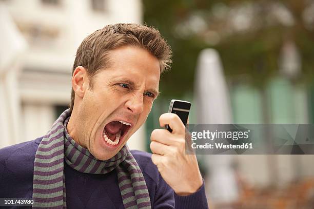 germany, bavaria, munich, man holding mobile phone, screaming, portrait - furioso imagens e fotografias de stock
