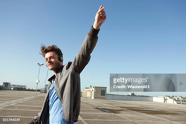 germany, berlin, young man on empty parking level wearing headphones - man with arms raised stock pictures, royalty-free photos & images