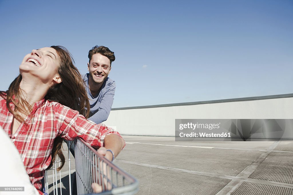 Germany, Berlin, Young man pushing young woman in shopping cart