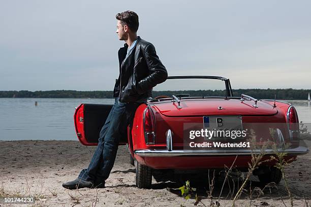 germany, berlin, lake wannsee, young man standing by car, looking over water, portrait - standing water fotografías e imágenes de stock