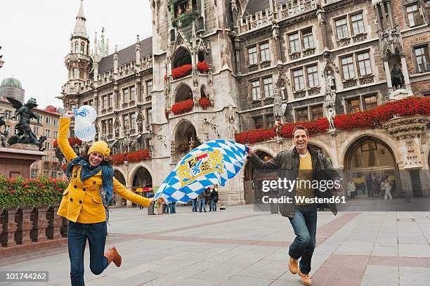 germany, bavaria, munich, couple running over place carrying balloons and bavarian flag, laughing, portrait - bavaria flag stock pictures, royalty-free photos & images