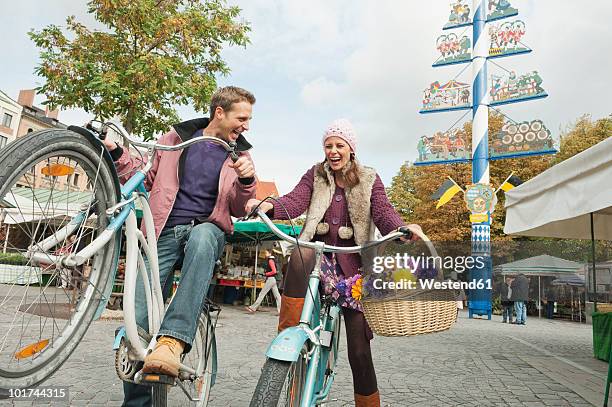 germany, bavaria, munich, viktualienmarkt, couple with bicycles, laughing, portrait - maibaum münchen stock-fotos und bilder