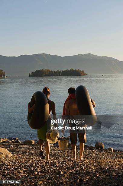a young couple prepare to float on the lake in inner tubes during a hot summer day. - pend orielle lake stock pictures, royalty-free photos & images