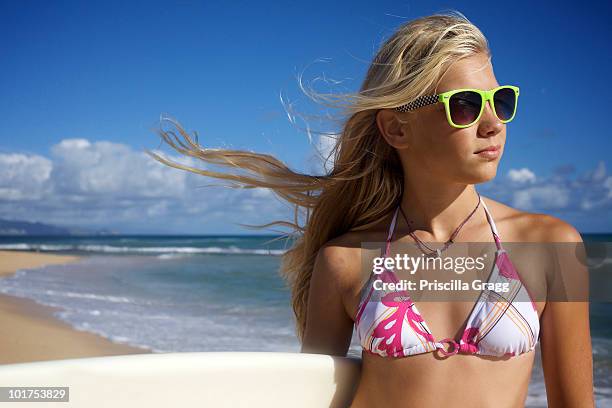 a pre-teen surfer girl wearing sunglasses poses for the camera at paia beach, maui, hawaii as her hair is being blown by the wind. - junge 13 jahre oberkörper strand stock-fotos und bilder