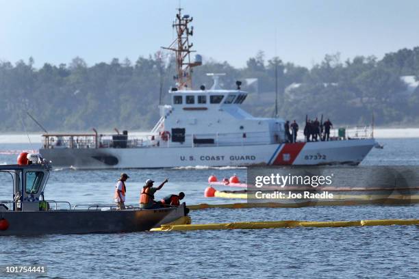 Coast Guard boat passes as workers put oil containment booms in the water as they try to protect the inlet waterways from the Deepwater Horizon oil...