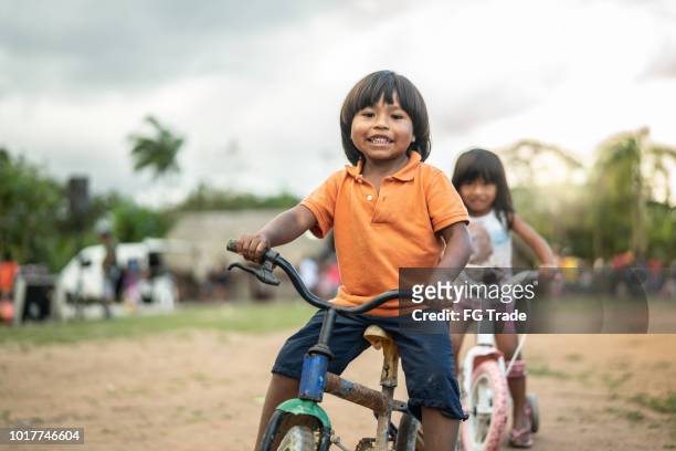 twee kinderen een fiets in een landelijke plaats - inheemse bevolking stockfoto's en -beelden
