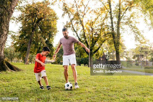 père apprend à son fils comment jouer au football - family garden play area photos et images de collection