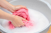 Woman hand washing knitted woolen laundry in grey plastic basin.Lot of soap white detergent. Dry skin and irritation