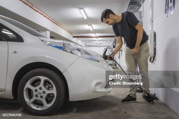 An employee connects an electric charging plug to a Nissan Motor Co. Leaf electric automobile, operated by ride-sharing startup CleverShuttle, in...