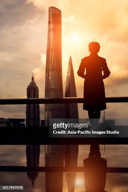 rear view of beautiful asian businesswoman looking at city of shanghai, the background is skyscrapers and landmarks of shanghai, including shanghai tower, shanghai world financial center and jin mao tower. - businesswoman silhouette stock pictures, royalty-free photos & images