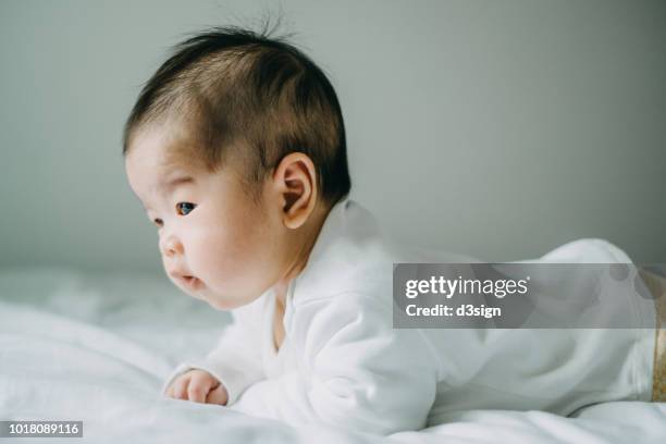 cute baby girl lying on her stomach on bed learning to crawl - prono foto e immagini stock
