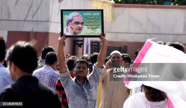 Worker raise a poster of former Prime Minister Atal Bihari Vajpayee as he waits for Vajpayees mortal remains to reach the BJP headquarters, on August...