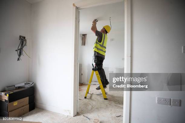 An electrician fits a smoke alarm inside a newly built home at a Persimmon Plc residential construction site in Grays, U.K., on Tuesday, Aug. 14,...