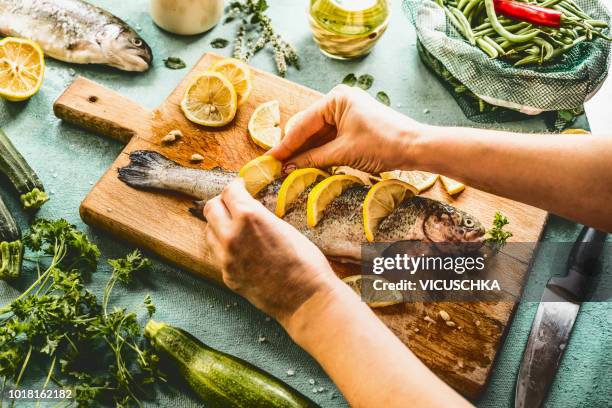 female woman hands stuff with lemon raw trout fishes - preparación de alimentos fotografías e imágenes de stock