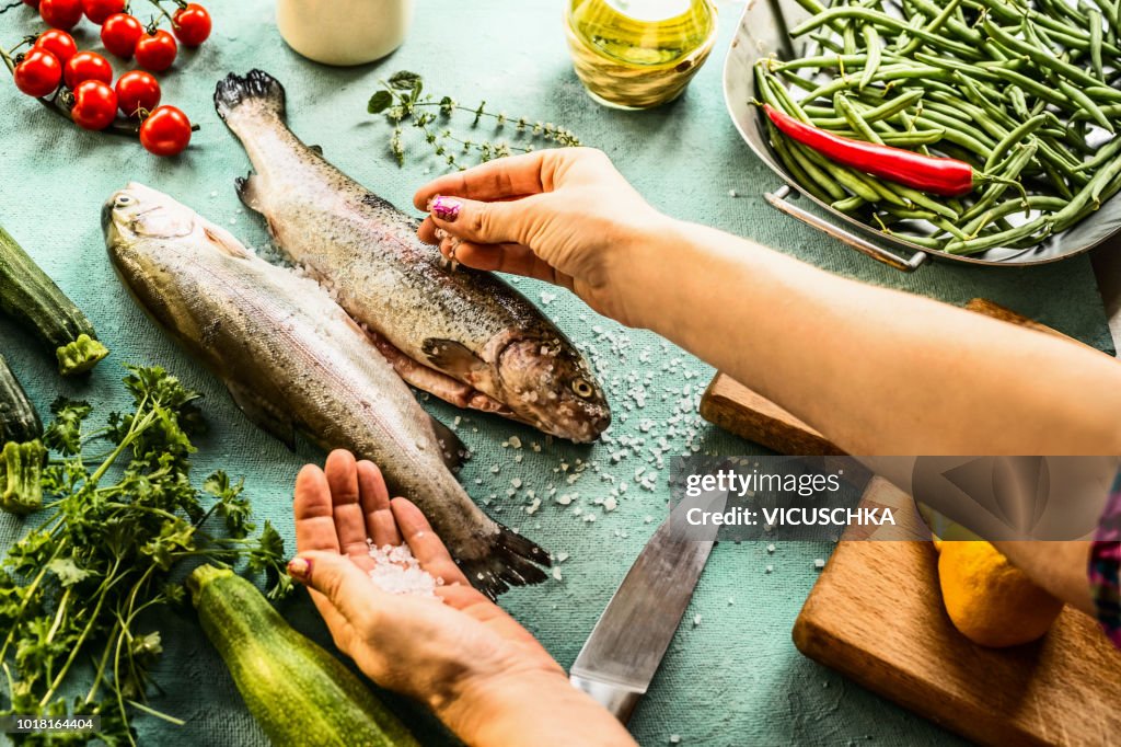 Female woman hands sprinkle with salt raw trout fishes