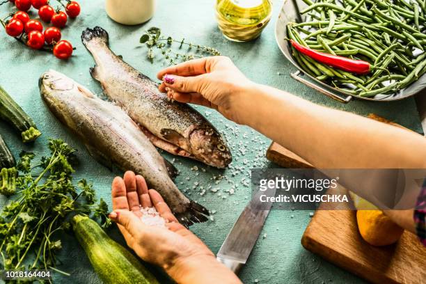 female woman hands sprinkle with salt raw trout fishes - trout stock photos et images de collection