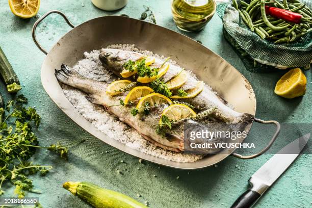 two trout stuffed with herbs and lemon slices in fish pan - forel stockfoto's en -beelden