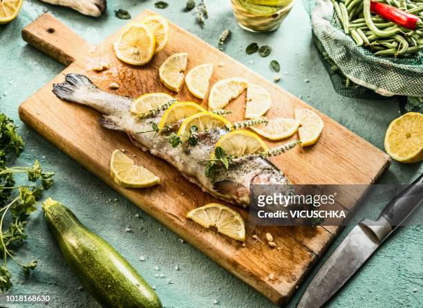 raw trout fish on cutting board stuffed with herbs and lemon slices - fische stock-fotos und bilder
