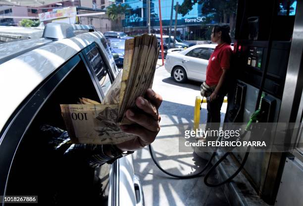 Customer shows Bolivar bills while at a gas station in Caracas where people queueing for petrol on August 17, 2018 for the uncertainty about the...