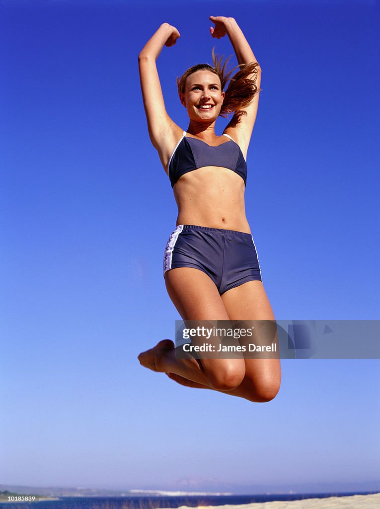 WOMAN IN SWIMWEAR JUMPING ON BEACH, CLOSE-UP