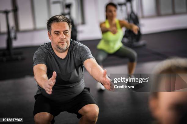 übergewicht im mittleren alter mann macht kniebeugen im aerobic-kurs - chubby men stock-fotos und bilder