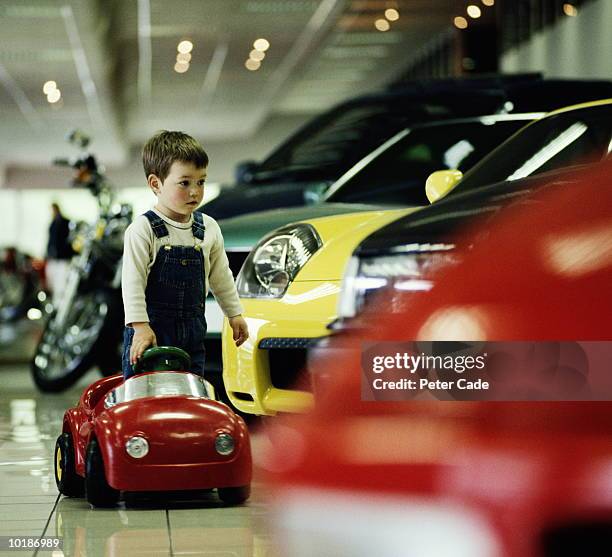 boy (3-5) with toy car in car showroom - the big dream stock pictures, royalty-free photos & images