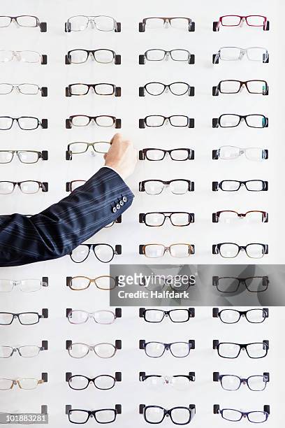 a human hand choosing a pair of glasses in an eyewear store - buying eyeglasses stock pictures, royalty-free photos & images