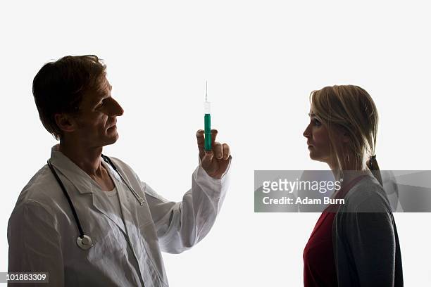 a doctor holding up a syringe facing a worried patient - doctor in silhouette stock pictures, royalty-free photos & images