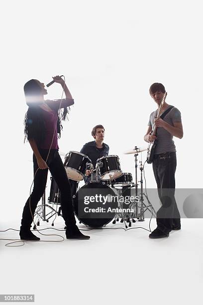 a drummer, guitarist and singer performing, studio shot, white background, back lit - rock musician foto e immagini stock