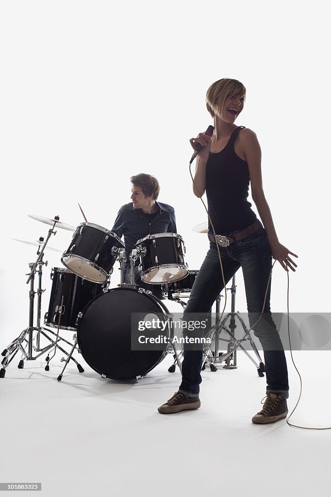 A female singer and a man on drums performing, studio shot, white background, back lit