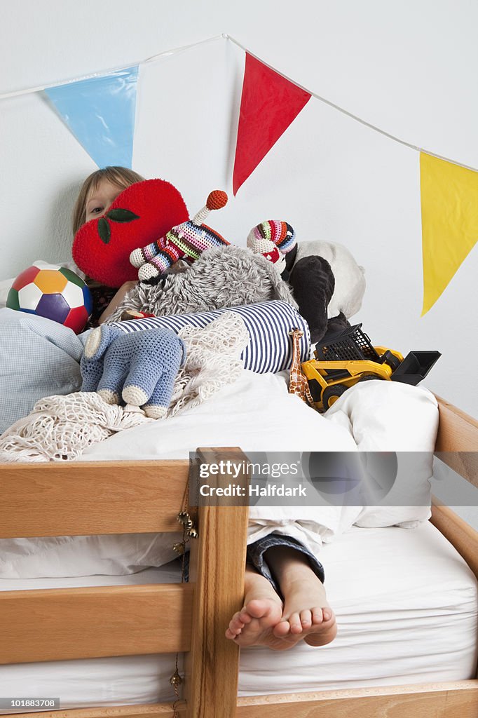 A young girl lying on a bunk bed covered in stuffed toys