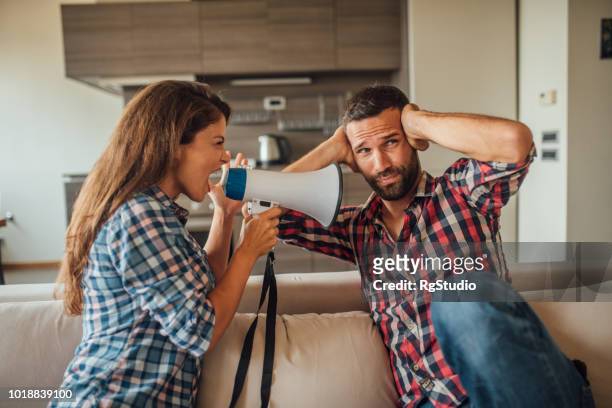 young man covering his ears while a woman yells at hm through megaphone - stubborn stock pictures, royalty-free photos & images