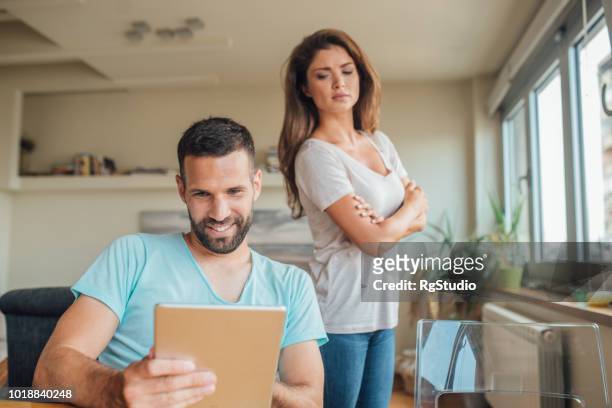 junge frau, die eifersüchtig auf den lächelnden mann mit digital-tablette - cheating wife stock-fotos und bilder